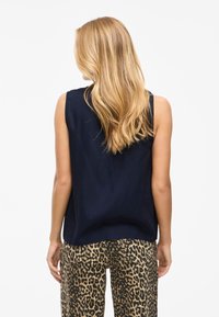 Top sin mangas en color marino con un corte holgado, combinado con pantalones de estampado de leopardo en una tela texturizada y con bolsillos traseros.