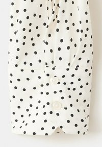 Weißer Stoffärmel mit schwarzen Punkten und zwei weißen Knöpfen in der Nähe der Manschette.