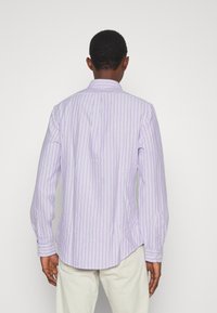 Chemise à manches longues en tissu violet clair avec des rayures verticales blanches. Dotée d'un col classique et de poignets à bouton. Détail d'ourlet courbé.