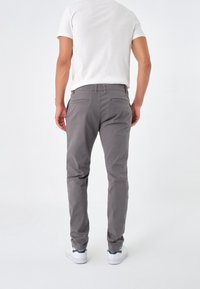 Grå bomullsblandning byxor med slim fit, med bakfickor och en jämn textur, iklädda med en vit t-shirt och vita sneakers.