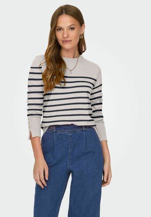 Pull rayé gris clair avec des rayures marines, doté d'un col rond et de boutons décoratifs aux poignets. Porté avec un pantalon en denim taille haute.