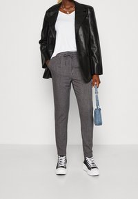 Grå rutiga byxor med dragsko i midjan, ihop med en vit t-shirt och en svart läderblazer. Tillbehören inkluderar en liten blå väska.