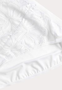 Vit lingeri med spetsöverdrag som har intrikata mönster, mjuk textur, elastiska kanter och en liten rosett som accent.