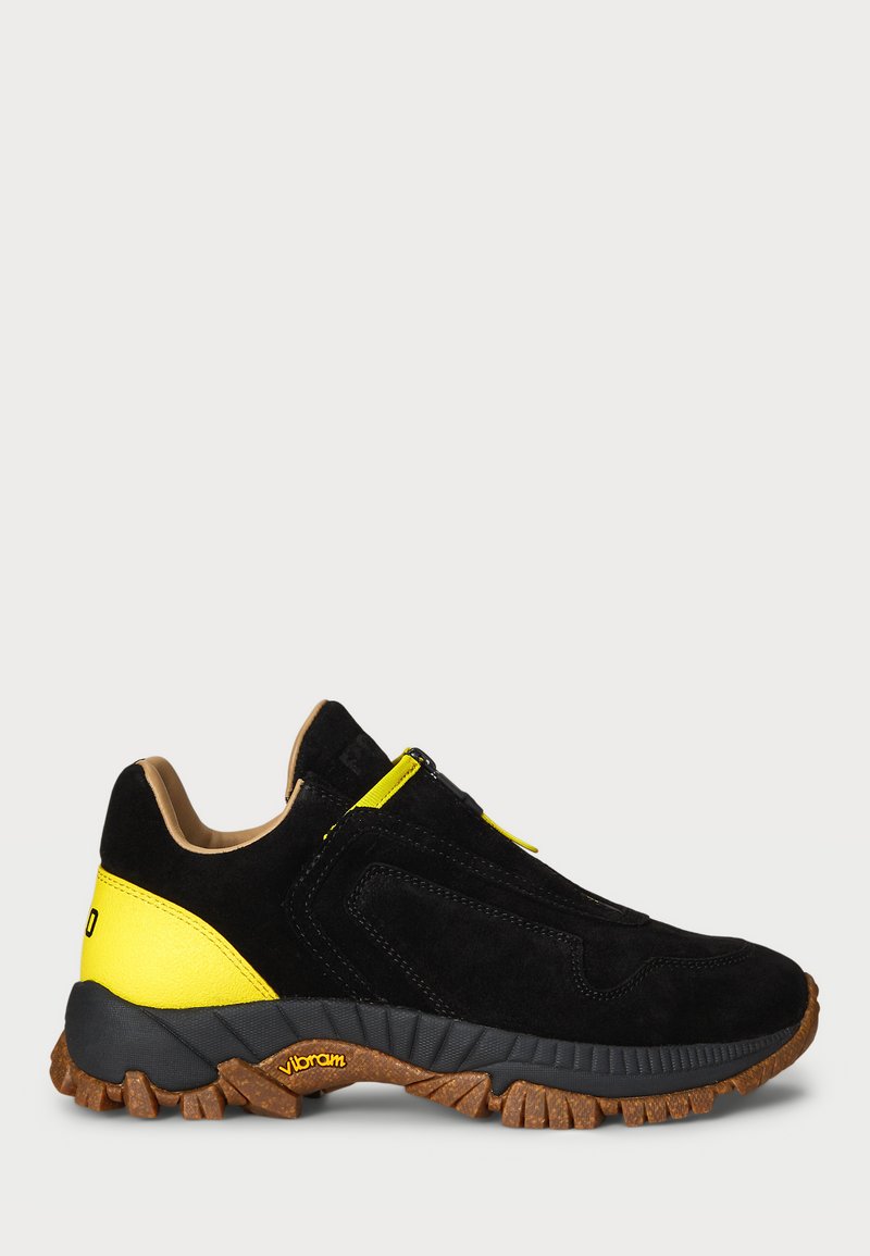 Melns zamšāds sneaker ar dzelteniem akcentiem, strukturētu gumijas zoli un gludu ādas mēli. Iekļauj ieelpojamo rāvējslēdzēju un Vibram zīmolu.