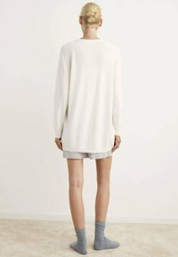 Maglione bianco a maglia con maniche lunghe, vestibilità ampia e orlo a coste. Abbinato a pantaloni corti a righe e calze grigie al ginocchio.