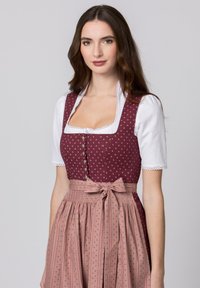 Traditionelles Dirndlkleid mit einem burgunderfarbenen Mieder mit Punkten, einer weißen Bluse und einem knielangen rosa Rock mit einer Schleife an der Taille.