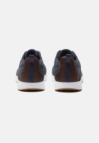 Morskie buty sportowe z brązowymi skórzanymi akcentami, białą podeszwą i teksturowanym wierzchem. Pętla do zakupu z tyłu i smukły design.