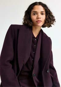 Mørkeblå skræddersyet blazer med store klapper, dobbeltknaplukning og et tekstureret stof, lagd over en matchende skjorte med knapper.