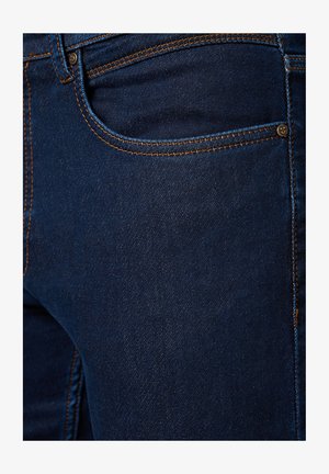 Granatowe dżinsy z pomarańczowymi przeszyciami, z przednią kieszenią i gładką fakturą. Zawierają metalowy detal z guzikem obok kieszeni.