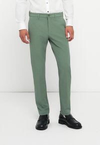 Green tailored pants made of smooth fabric, featuring a straight leg design, side pockets, and a button closure. Worn with black shoes.
