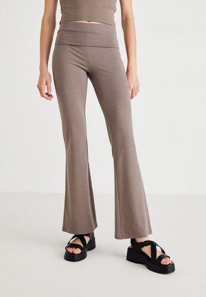 Brune flared leggings med bred taljeelastik, lavet af strækstof; parret med sorte plateau sandaler med krydsede stropper.