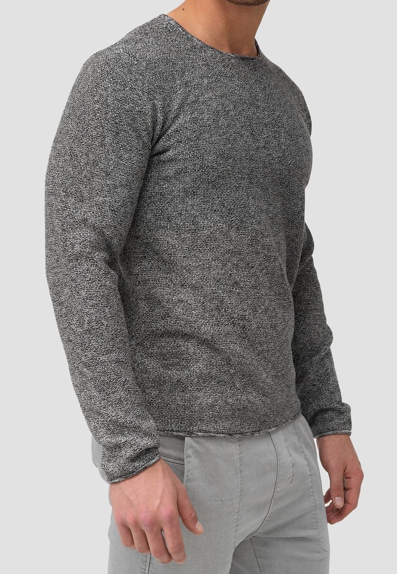Maglione grigio a maglia con maniche lunghe e collo rotondo, caratterizzato da una finitura testurizzata e polsini a costine, abbinato a pantaloni grigio chiaro.