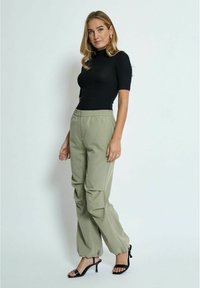 Top negro ajustado de manga corta combinado con pantalones cargo de fit relajado en un tono oliva claro, con bolsillos laterales y puños de pierna ajustados. Tacones negros.