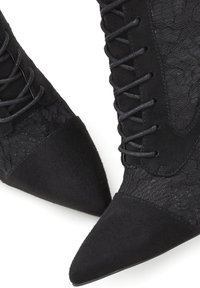 Botas negras hasta el tobillo con puntera puntiaguda, que presentan una mezcla de encaje texturizado y ante suave, adornadas con cordones negros.