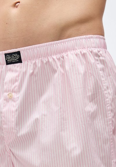 Κοντινή λήψη της μέσης ενός ατόμου που φορά ροζ ανοιχτόχρωμα ριγέ ελαστικά σορτς boxer με ετικέτα Polo RL Co. σε μαύρο χρώμα.