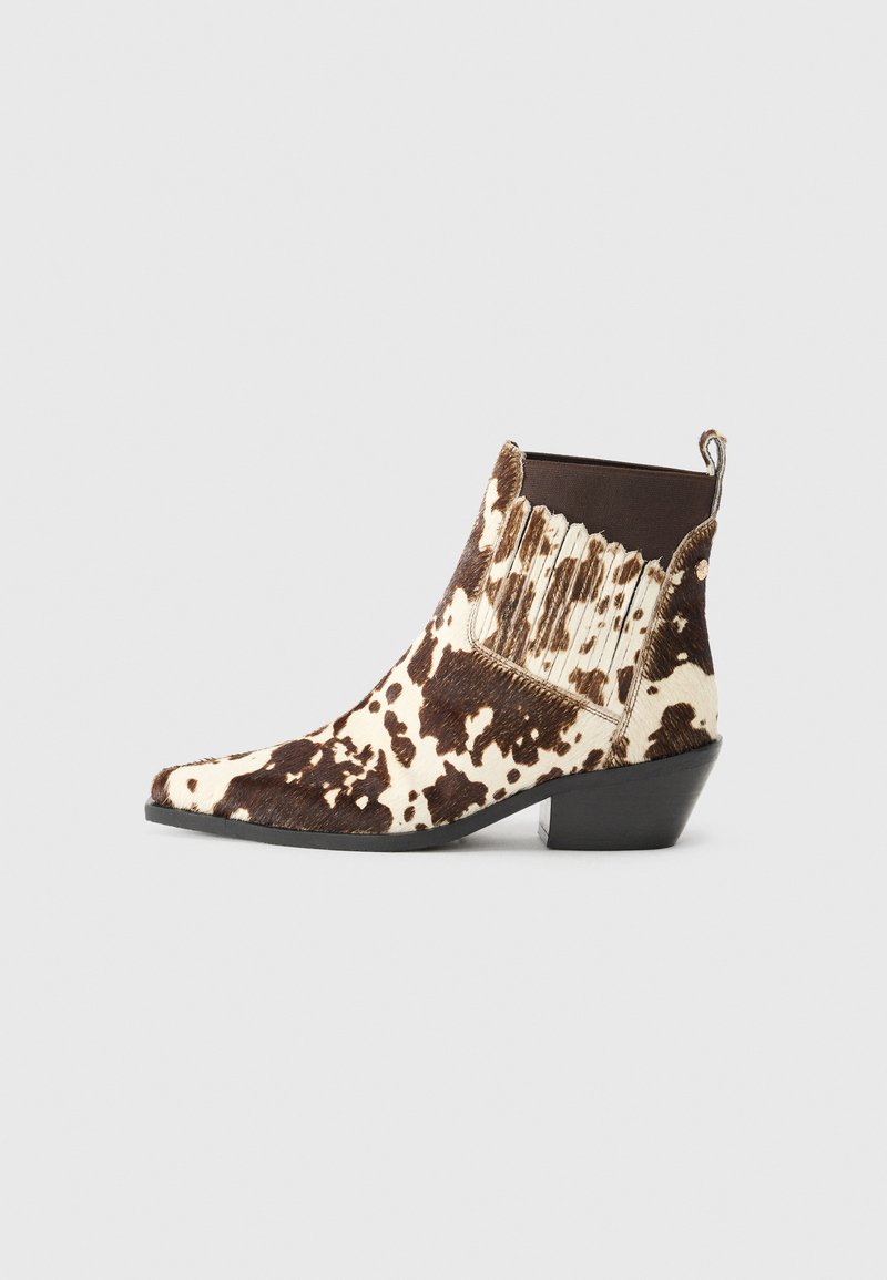 Kavbojske gležnjarje iz rjave in smetane barve krzna, z ostrim nosom, nizko peto in rebrasto okrasitev na straneh.