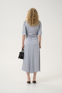 Light blue, knee-length dress with short puff sleeves, a gathered back, and a flowing skirt. Paired with a small black handbag and heels.