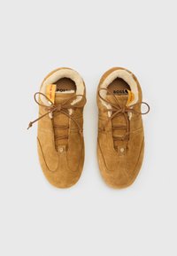 Tênis de camurça bege com forro de pelagem suave, atacadores planos e um design costurado. Pequeno detalhe do logótipo de lado e uma etiqueta brilhante no interior.