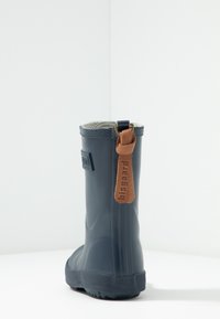 Bota de lluvia de goma navy con suela texturizada, etiqueta de cuero marrón claro y forro suave en gris, que presenta un acabado liso y altura hasta la pantorrilla.