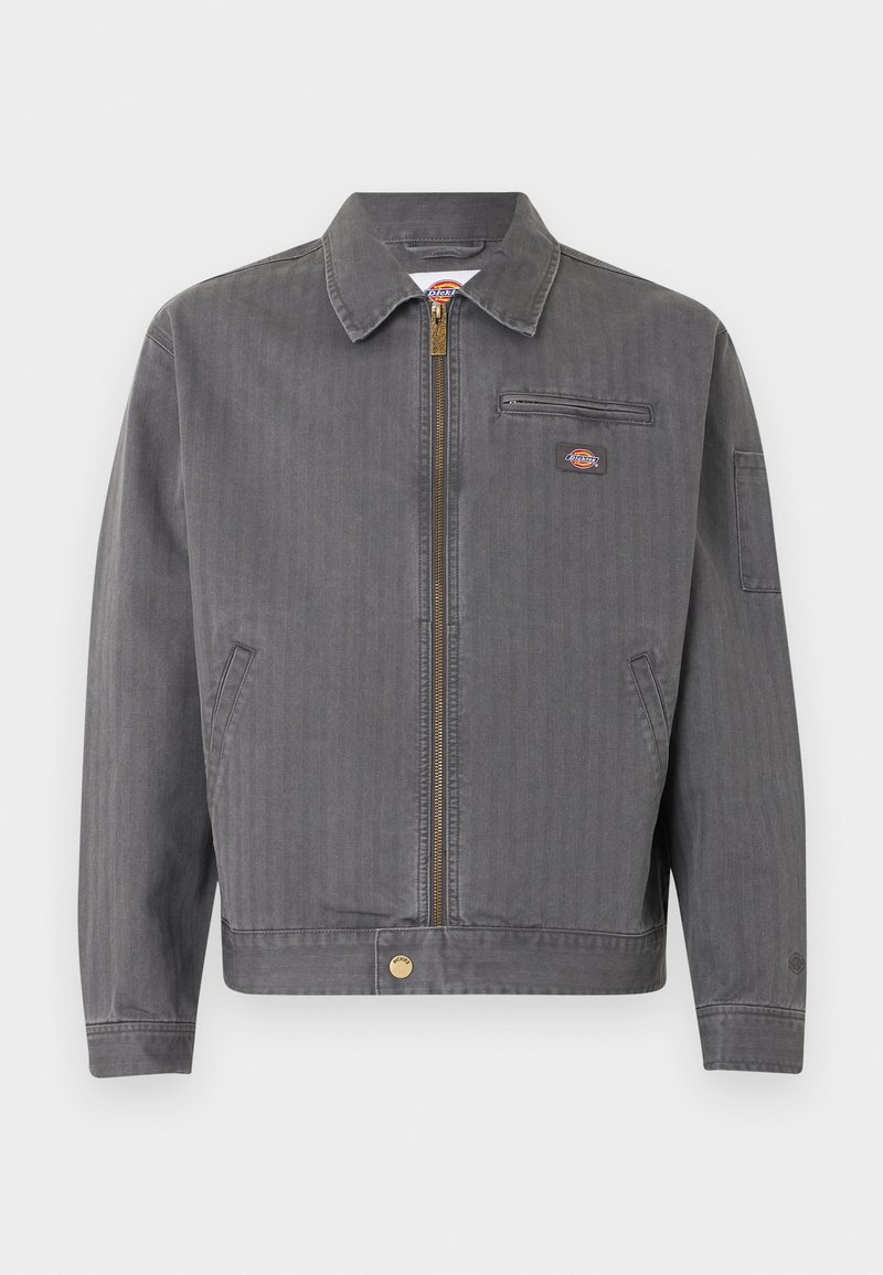 Graue Arbeitsjacke zum Reißverschluss mit Kragen, Brusttasche mit Reißverschluss, Seitentaschen und kleinem Logoaufnäher auf Brust und Ärmel.