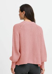 Rosa stickad tröja med lös passform, ribbat mönster och långa, puffiga ärmar. Har en rundad halsringning och en något croppad bakdel.