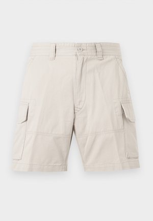 Μπεζ cargo σορτς με μπροστινό κουμπί και φερμουάρ, θηλιές για ζώνη, πλαϊνές τσέπες με καπάκι και μήκος μέχρι το γόνατο, εμφανιζόμενα σε απλό φόντο.