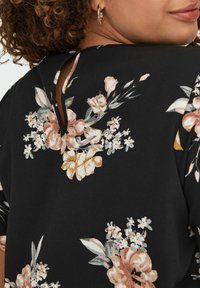 Blusa nera a fiori con un design a chiave sulla schiena, con fiori rosa e dorati dettagliati su un tessuto liscio. Accenti sottili e testurizzati arricchiscono il design.