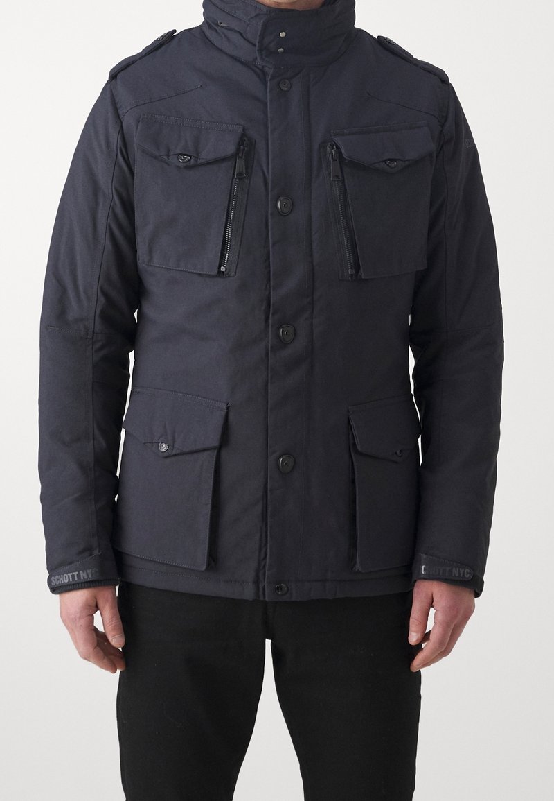 Chaqueta aislante de color azul marino con cuatro bolsillos frontales, bolsillos con cremallera en el pecho y cierre de botones. Cuenta con un cuello alto y tejido texturizado.