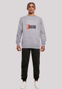 Gray sweatshirt with ribbed cuffs and hem, featuring a multicolored graphic design on the front. Paired with black jogger pants and white sneakers.