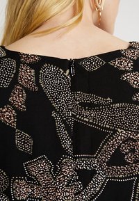 Schwarzer Stoff mit einem strukturierten Muster aus hellbraunen und grünen Blättern und Formen, mit einem dezenten Rückenzipper-Detail.