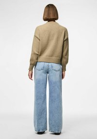 Khaki knit sweater with dropped shoulders and ribbed cuffs, paired with wide-leg light blue denim jeans featuring faded accents and back pockets.