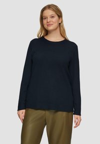 Diepblauwe longsleeve trui met een ronde hals, gemaakt van lichtgewicht stof en in een relaxte pasvorm, gecombineerd met olijfgroene broeken.