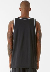 Melnā sporta topiņš ar baltām apdari apkaklītei un rokām. Iespējota sniegta auduma struktūra gaisa caurlaidībai, apakšmalai atrodas zem jostas.