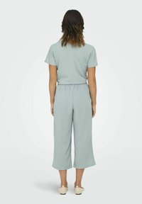 Ljusgrön byxdress med avslappnad passform, korta ärmar, elastisk midja och vida ben. Slätt tyg utan synliga mönster.