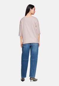 Hellbeige Oversized-Hemd mit Dreiviertelärmeln, kombiniert mit lockeren blauen Jeans aus Denim mit dekorativen Nähten und Leopardenmuster-Absatzschuhen.