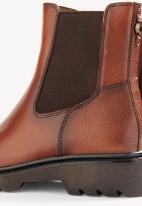 Brown leather Chelsea boot, featuring elastic side panels, textured accents, a rounded toe, and a sturdy lug sole for traction.