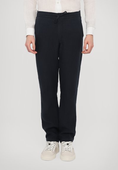 Marineblauwe linnen broek met een trekkoord in de taille, rechte pasvorm en subtiele textuur. Gecombineerd met witte sneakers met zwarte veters en accenten.