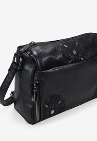 Bolso cruzado de piel negra con detalles florales bordados en verde y plata. Presenta un cierre de cremallera y una correa ajustable.