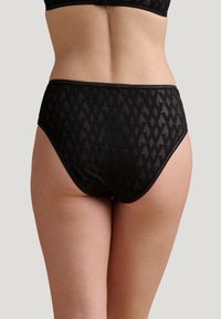 Zwarte kanten slip met geometrisch patroon, hoge taille, gladde textuur en contrasterende stiksels langs de tailleband en beenopeningen.
