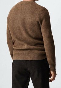 Maglione a coste marrone con scollo rotondo, maniche lunghe e silhouette aderente, abbinato a pantaloni scuri e texturizzati.