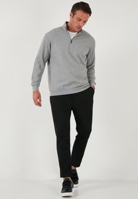 Light gray zip-up sweatshirt with a textured pattern, paired with black tapered pants and black sneakers. Features a high neckline and ribbed cuffs.