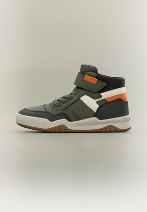 Højtop-sneaker i grøn, sort og hvid med orange accenter, snørebånd og velcrolukning over anklen på en neutral baggrund.