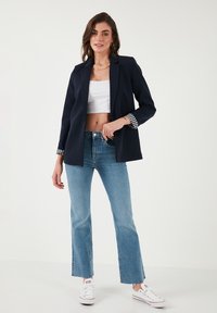 Mornarsko modra blejzer s prugastimi manšetami, nosen prek bele skrajšane majice in svetlo modrih širokih jeans hlač, v kombinaciji z belimi supergami. Preprost, čist dizajn.