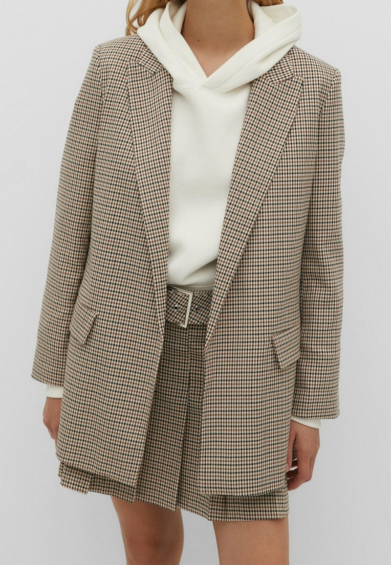 Blazer à carreaux en tissu léger aux tons beige et marron, assorti d'un sweat à capuche blanc et d'un short à carreaux assorti. Doté d'une ceinture en guise d'accent.