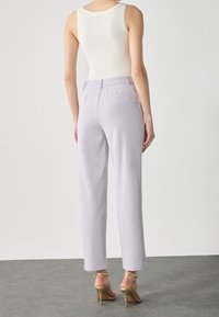 Ljuslila byxor med skräddarsydd passform, slät front och bakfickor. Bärs med ett åtsittande vitt linne och guldig klackar med remmar.