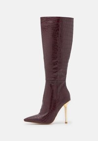Pitsin korku burgundi värviga faux krokodillederist saapad, millel on terav varvas ja kuldne stiletto konts. Siledat tekstuuri ja sujuvat disaini.