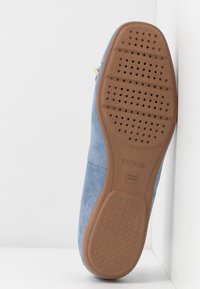 Chaussure plate en daim bleu avec une semelle en caoutchouc marron dotée de trous de ventilation et d'une texture lisse. Design minimaliste sans aucun élément métallique apparent.
