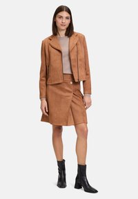 Brown faux suede jacket with zip closure, paired with a matching brown skirt featuring a button detail and asymmetrical hem. Black ankle boots.