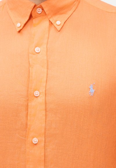 Πορτοκαλί πουκάμισο με κουμπιά και γιακά με κουμπιά, με μικρό λευκό κεντητό λογότυπο παίκτη πόλο στο αριστερό στέρνο.