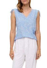 Donna che indossa un top senza maniche di un leggero blu chiaro con motivi floreali bianchi e spalline annodate, abbinato a pantaloni bianchi larghi.